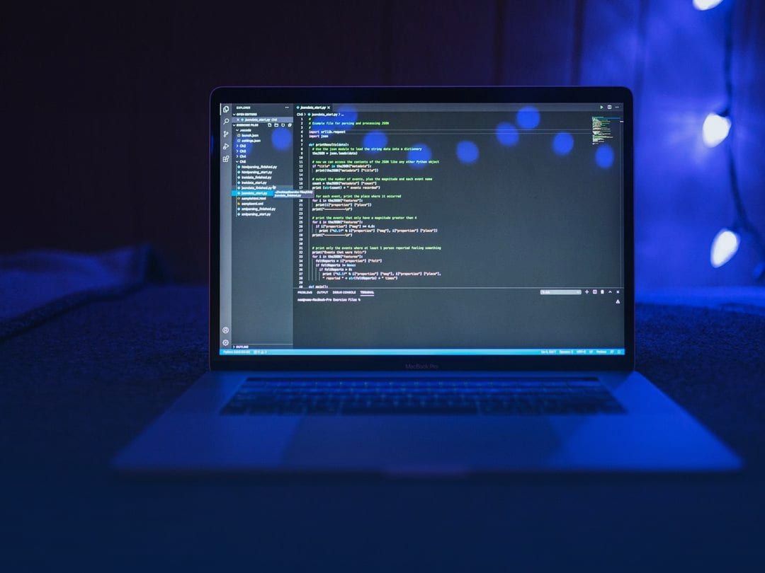 Laptop in a dark room showing program code, lit by blue lights