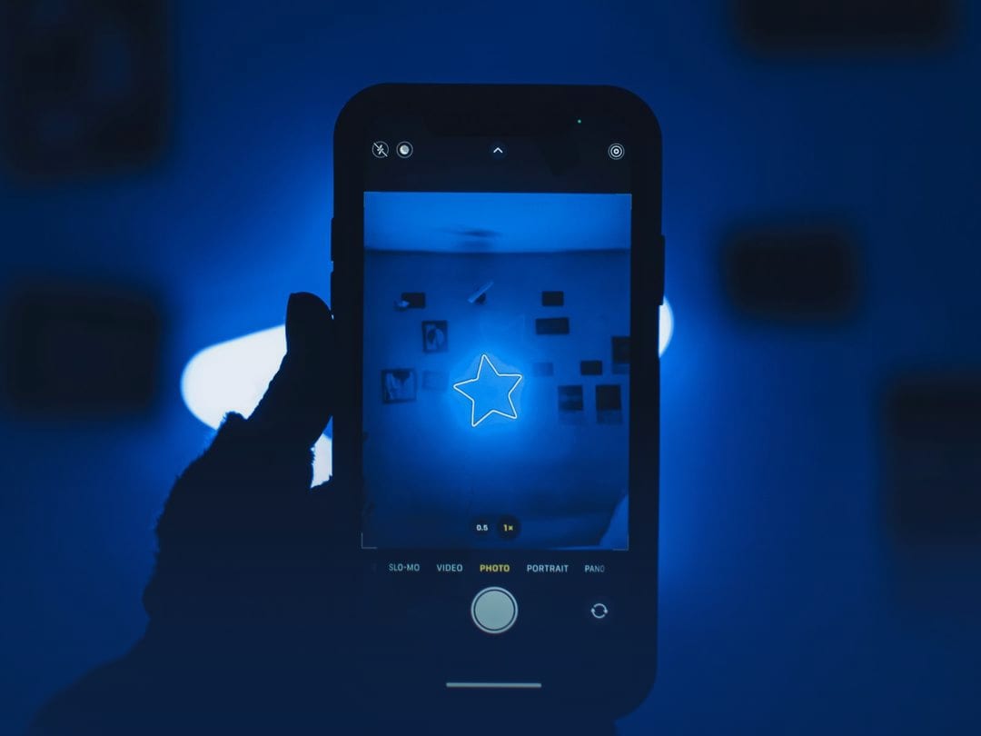 Hand holding a smartphone against a deep blue background, with a glowing star on its screen